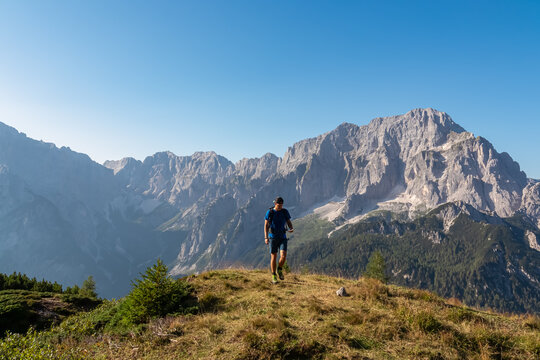 Active hiker man on alpine meadow with scenic view of rugged mountain peak Jof di Montasio. Majestic ridges of Julian Alps in Somdogna, Friuli Venezia Giulia, Italy. Wanderlust Italian Alps in summer
