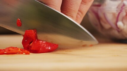 Close-up chopping red hot chilli peppers with sharp knife on cutting board, juicy fresh red hot chilli pepper