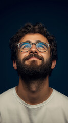 Obraz premium Portrait of a happy man with a beard and glasses looking up, against a solid dark blue background. 