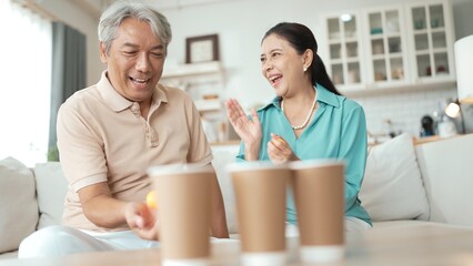 Obraz premium Happy elderly couple enjoying a ball toss game together at home, practicing coordination and cognitive skills for healthy aging. Grandfather and grandmother throwing ping pong in the bowl. Myrmidon.