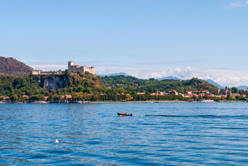 Fototapeta premium From Arona, the Rocca di Angera rises majestically above Lake Maggiore, its medieval fortress perched on a hill, offering a stunning contrast to the serene waters below.
