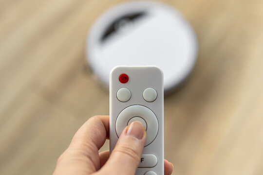 A man or woman holds a remote control for controlling a robot vacuum cleaner. Natural