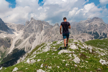 Naklejka premium Hiker man on top of Cima Sophia with panoramic view of majestic cloud covered rugged mountain peaks of Brenta Dolomites, Trentino, Italy. Summer wanderlust in alpine wilderness Italian Alps. Freedom