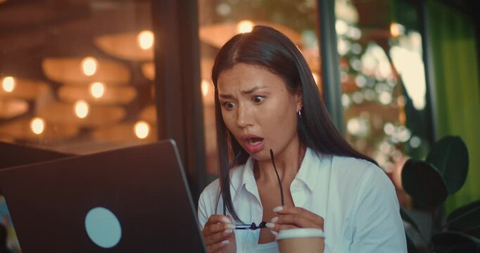 Young adult woman in eyeglasses at computer visibly distressed and frustrated, indicating high work-related stress. Stunning female at laptop displaying visible distress and frustration.