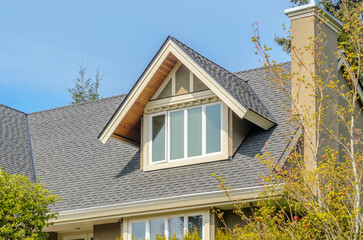 Top of grey stucco luxury house with shingle roof, red and yellow trees and nice windows in Summer...