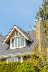 Top of grey stucco luxury house with shingle roof, red and yellow trees and nice windows in Summer in Vancouver, Canada, North America. Day time on June 2024.