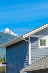 Top of grey stucco luxury house with shingle roof, red and yellow trees and nice windows in Summer in Vancouver, Canada, North America. Day time on June 2024.