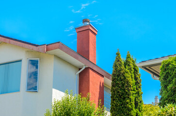Top of grey stucco luxury house with shingle roof, red and yellow trees and nice windows in Summer in Vancouver, Canada, North America. Day time on June 2024.