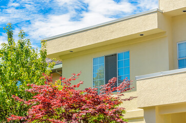 Top of grey stucco luxury house with shingle roof, red and yellow trees and nice windows in Summer in Vancouver, Canada, North America. Day time on June 2024.