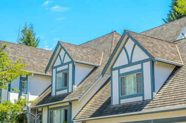 Top of grey stucco luxury house with shingle roof, red and yellow trees and nice windows in Summer in Vancouver, Canada, North America. Day time on June 2024.