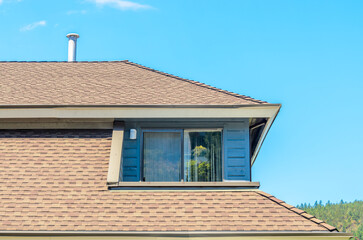 Top of grey stucco luxury house with shingle roof, red and yellow trees and nice windows in Summer in Vancouver, Canada, North America. Day time on June 2024.