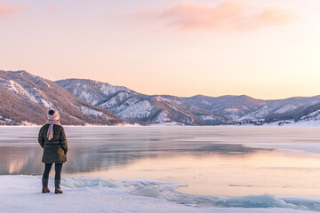 scenic winter view of Loch Ness in the Scottish Highlands, with snow-covered hills in the background and mist rising from the lake. A lone hiker stands on the edge of the lake, looking out at the tran