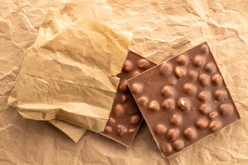 Dark chocolate with hazelnuts on kraft paper, close-up, top view.