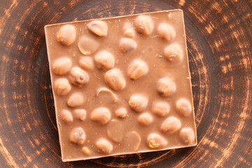 Dark chocolate with hazelnuts on a clay plate, close-up, top view.
