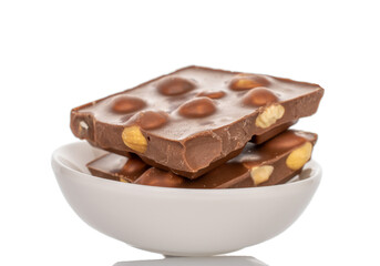 One bar of dark chocolate with hazelnuts in a ceramic dish, close-up, isolated on a white background.