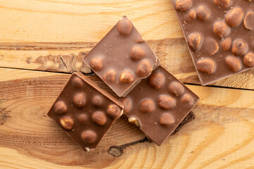 Dark chocolate with hazelnuts on a wooden table, close-up, top view.