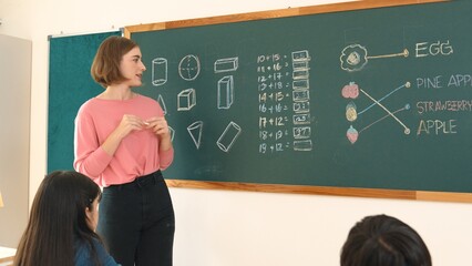 Caucasian student writing blackboard to answer math question at classroom while receive chalk and...