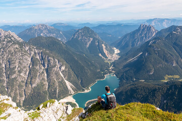 Hiker man on top of Cima Del Lago with aerial view of alpine lake Lago Del Predil in Val Canale...