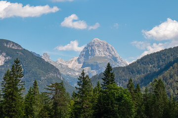 Scenic view of majestic mountain peak Mangart surrounded by coniferous forest in remote Julian...