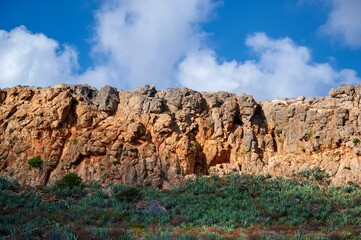Tall rocky wall and green vegetation under blue sky in ismall island Gramvousa, Crete.