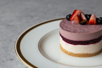 Blueberry cheesecake with fresh berries on a white plate on a gray background