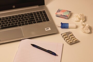 Working while sick; In the background there is a laptop, notebook, tissues, nasal spray and pills