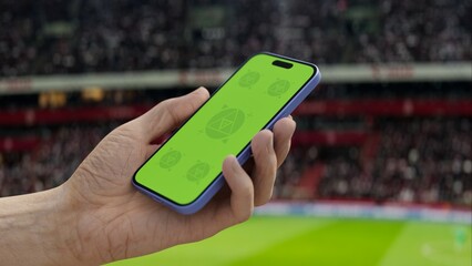 GREEN SCREEN CHROMA KEY A hand holding a phone with a green screen at a stadium during a football...