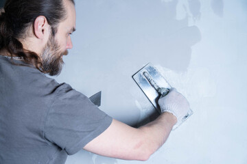 A person smoothly spreads epoxy adhesive or decorative plaster on a wall using a trowel in a workshop setting.