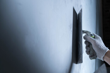 A hand with a glove is using a trowel to apply epoxy adhesive on a wall surface for repair. Microcement or decorative plaster.