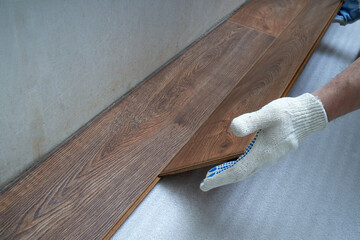 Men's gloved hands lay laminate flooring. Front view. The concept of repair and maintenance
