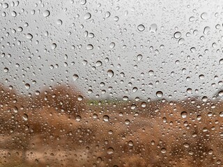 Water drops on the glass, rain is pouring through the window, beautiful droplets, fields