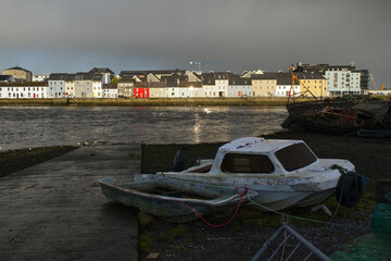 Naklejka premium Beautiful cityscape sunrise scenery with old wooden boat in Corrib river at Claddagh in Galway city, Ireland, architecture background