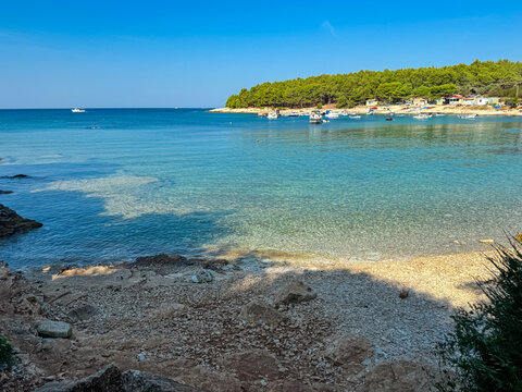 Panoramic view of boats floating in idyllic bay Uvala Polje in Cape Kamenjak National Park near Premantura, Istria, Croatia. Tropical vacation atmosphere in summer. Clear blue sky at the seaside