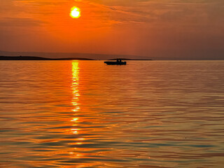 Fiery sunrise with fishing boat near island Otocic Trumbuja in bay Kamenjak national park, Adriatic Mediterranean Sea, Croatia. Seen from coastal town Premantura, Istria peninsula, Europe