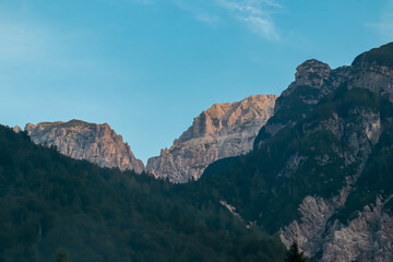 Scenic view of majestic mountain peak of Mangart in Julian Alps seen from Predil Pass, Tarvisio, Italy. Ridges covered in morning mist. Hiking trail on alpine terrain covered with conifer forest