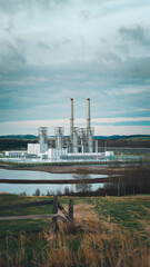 Obraz premium A modern power plant with multiple chimneys and industrial buildings, surrounded by greenery and roads, under a sky.