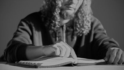 A curly-haired man sits in a prayer room, reading the Christian Bible with focus, tracing the text with his finger, and praying earnestly. A scene of faith, seeking answers, and spiritual devotion