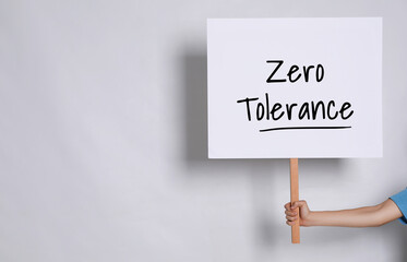 Woman holding sign with words Zero Tolerance on light grey background, closeup. Space for text