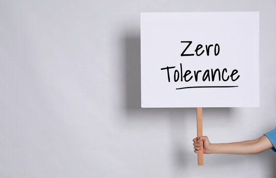 Woman holding sign with words Zero Tolerance on light grey background, closeup. Space for text