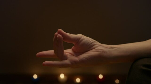 A close-up of a hand forming an apan meditative mudra against a softly lit background with blurred candlelights, creating a serene and calm ambiance perfect for mindfulness concept