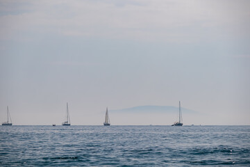 Lone sailing boats on horizon of shimmering Adriatic Mediterranean sea. Serene coastal scene with blue sky and calm turquoise water in Cape Kamenjak National Park, Istria, Croatia. Luxury vacation