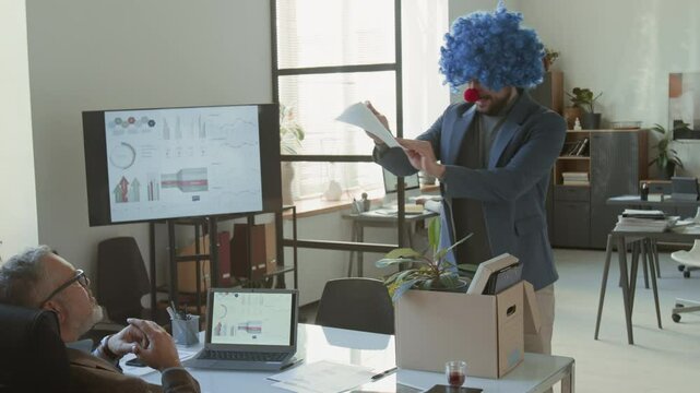 Fired businessman carrying box with his belongings, throwing resignation letter on table of boss, taking off clown wig and nose and leaving office