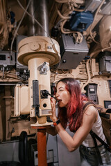 Young woman exploring submarine interior using periscope, experiencing naval history