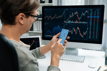 Smart stock investors pointing on screen with smartphone for market stock exchange along with laptop screen in highest dynamic investment rate, focusing data planning at modern workplace. Pecuniary.