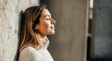 Fototapeta premium Young caucasian female relaxing against wall with closed eyes in natural light
