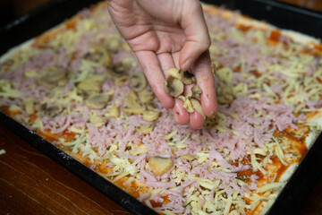 Woman's hand adding mushrooms on a pizza