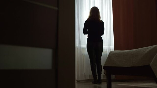 Sad and lonely woman standing at the window in the room. Concept of depression, problems and mental health. Female silhouette.