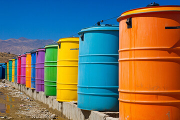 Colorful water storage barrels lined up against a clear blue sky in a rural area