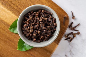 Dry clove buds in a small bowl macro. Whole organic cloves spice in a gray ceramic bowl on a cutting board. Spice, condiment, cooking concept. Close-up.