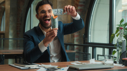 Happy male Arabian Indian business man crazy mad laughing guy joyful excited businessman office investor rejoicing fooling burn money dollars waste finance cash salary enjoy burning banknotes have fun